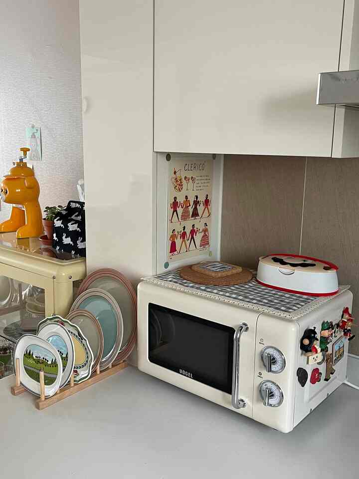 ナチュラルカラーとバターイエローが印象的なキッチン、レトロな電子レンジと木製皿立てが配置された雰囲気のあるインテリア