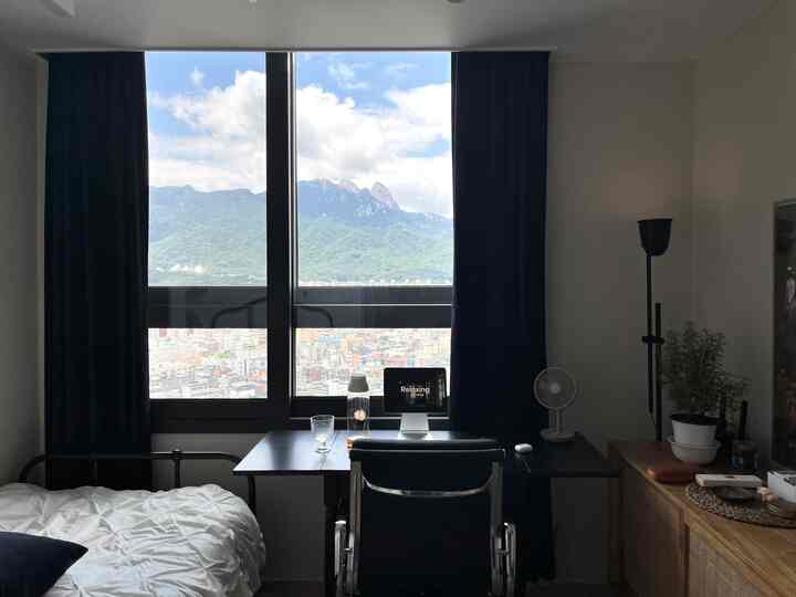 白とネイビーの色調のワンルーム寝室、窓際にデスクとオフィスチェアが配置された落ち着いた在宅勤務スペース