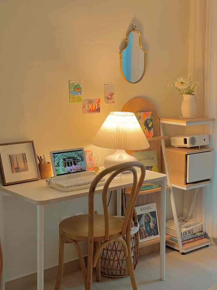 Cozy home office space featuring white and wood tones, a desk lamp on the table, and a decorative wall mirror