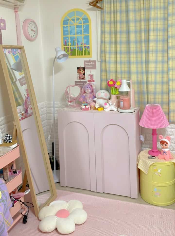 Pastel pink and yellow cozy interior space featuring a pink cabinet and yellow side table with cute decor elements