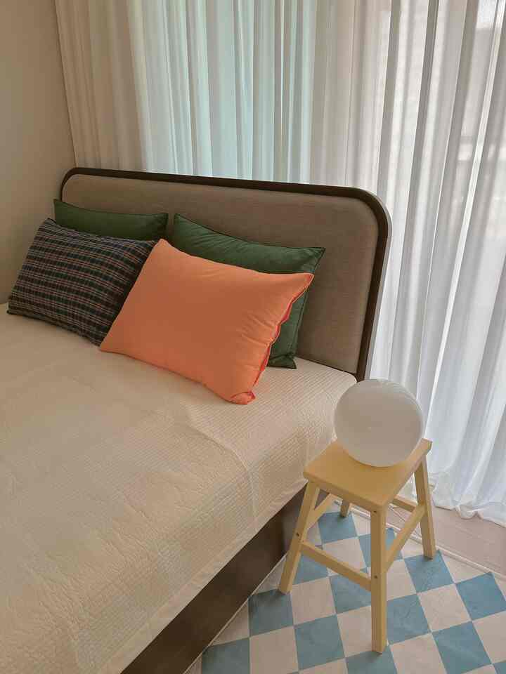 Bright bedroom with white and wood tones, featuring a yellow nightstand stool and green pillows creating a natural ambiance