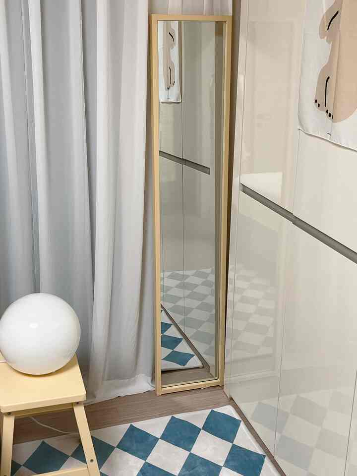 White and beige toned entrance space featuring a full-length mirror, curtains, blue checkered rug, and a small stool in a clean atmosphere