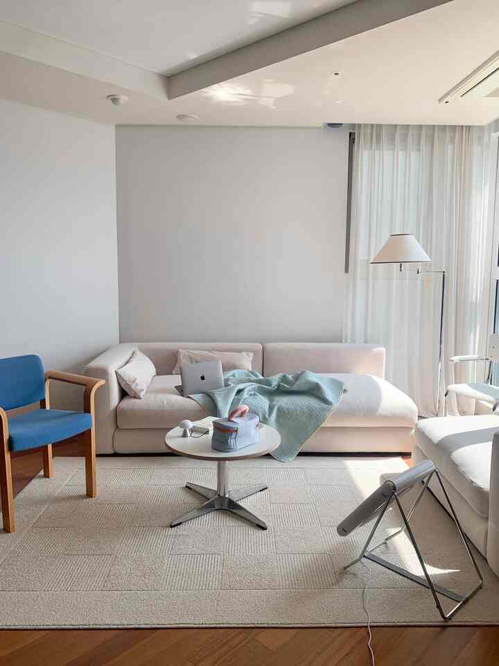 Bright natural-toned living room featuring cream sofa, blue armchair, round coffee table, and floor lamp in a simple setting