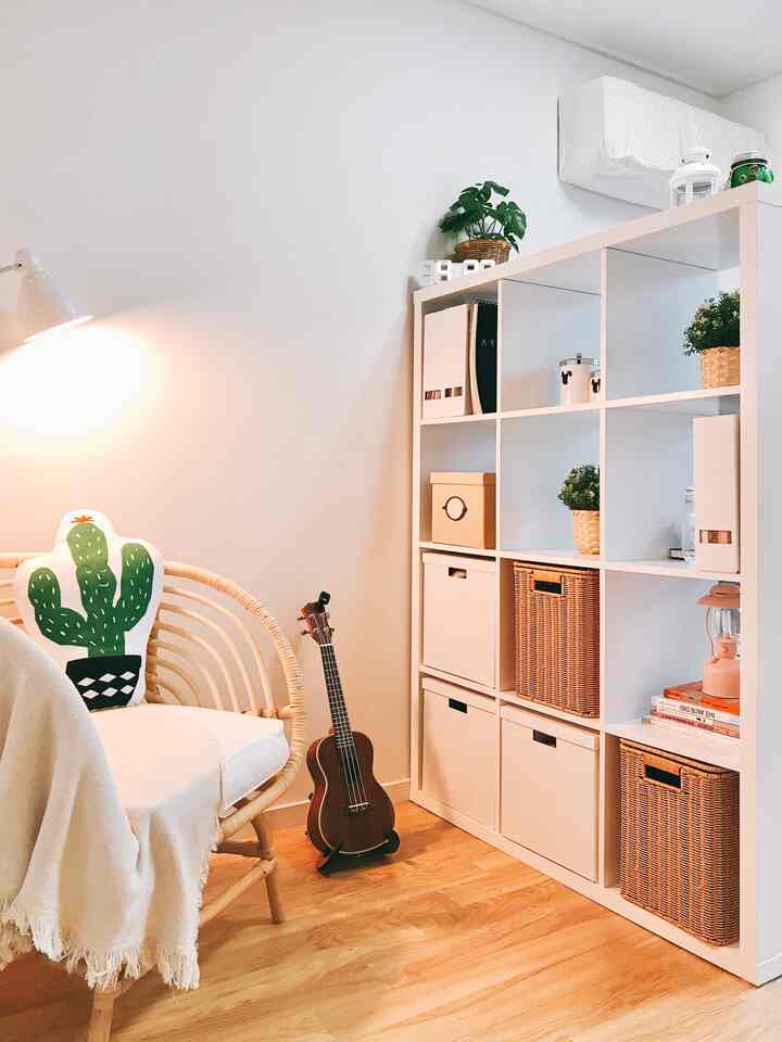 Natural color studio apartment featuring white shelving unit and rattan armchair with cozy atmosphere