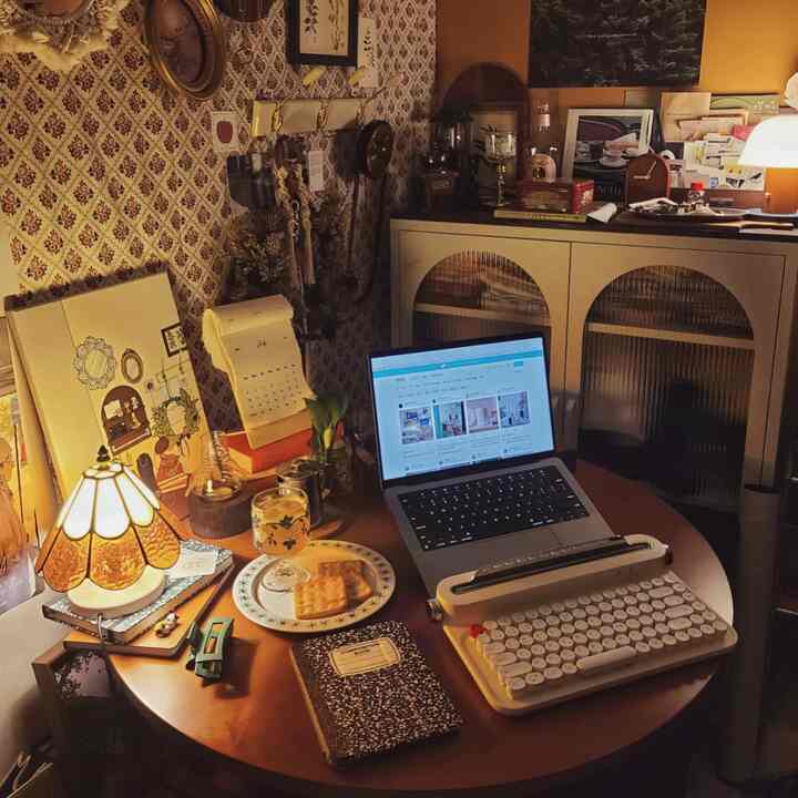 温かみのあるウッドトーンとヴィンテージムードのホームオフィス、丸テーブルにノートパソコンとレトロなタイプライターキーボードが配置された印象的な作業空間