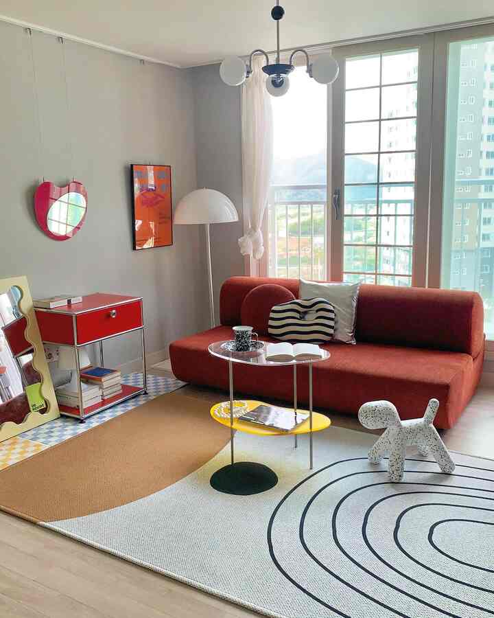 A modern living room with warm brown and red tones featuring a brick-red sofa, transparent coffee table, and geometric patterned rug