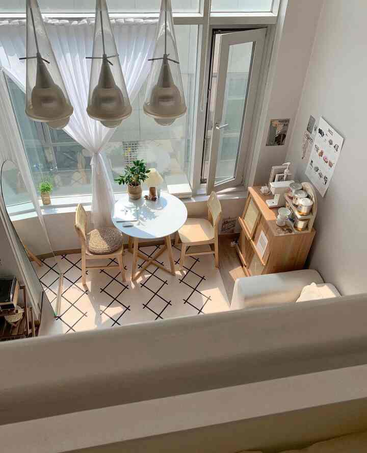 白と木目調のロフトリビング、円形テーブルとラタンチェア、キャビネットが配置された明るく居心地の良いおうちカフェ空間