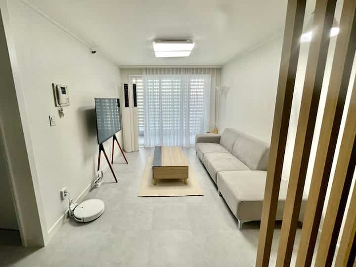 A small living room with white and wood tones, featuring a simple sofa and wooden table creating a spacious feeling