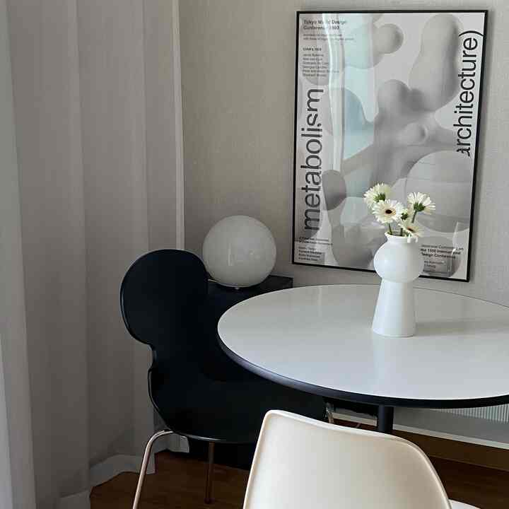 Black and white toned dining room featuring round table, chairs, vase with flowers, and poster in a clean modern interior