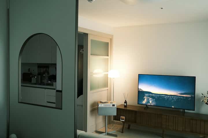 ホワイトと木目調が調和したモダンなリビング、テレビとフロアランプが配置された落ち着いた空間