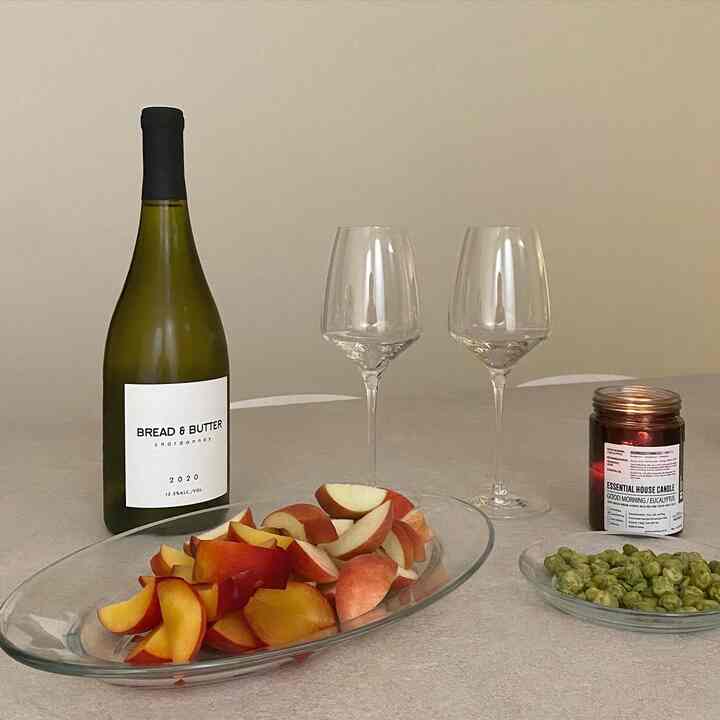 Beige-toned table featuring transparent wine glasses and plates, red fruit slices, a wine bottle, and a candle in a cozy home cafe setting