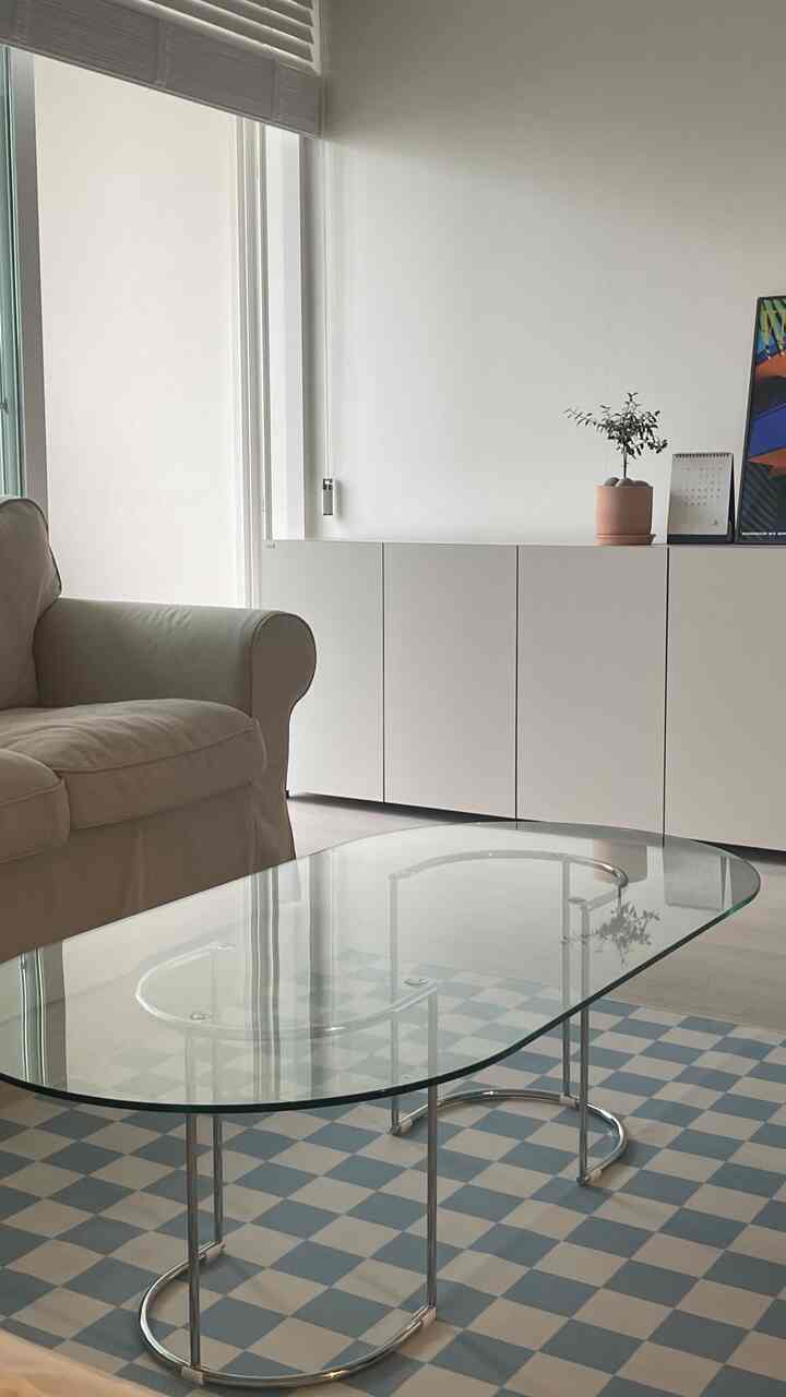 A white and sky blue toned living room featuring a white sofa, glass top coffee table, and a neat white storage cabinet, creating a simple atmosphere