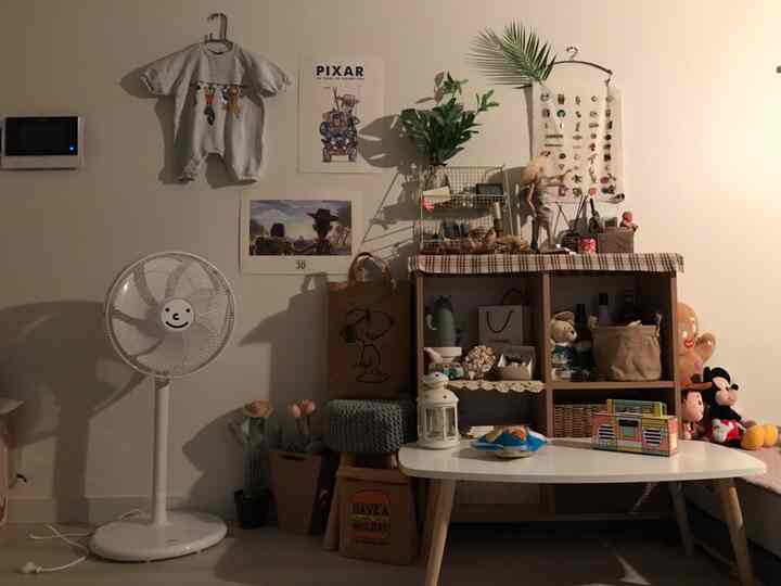 Studio apartment with white walls and brown furniture, featuring dolls, fan, stool and varied decor creating cozy single-living space