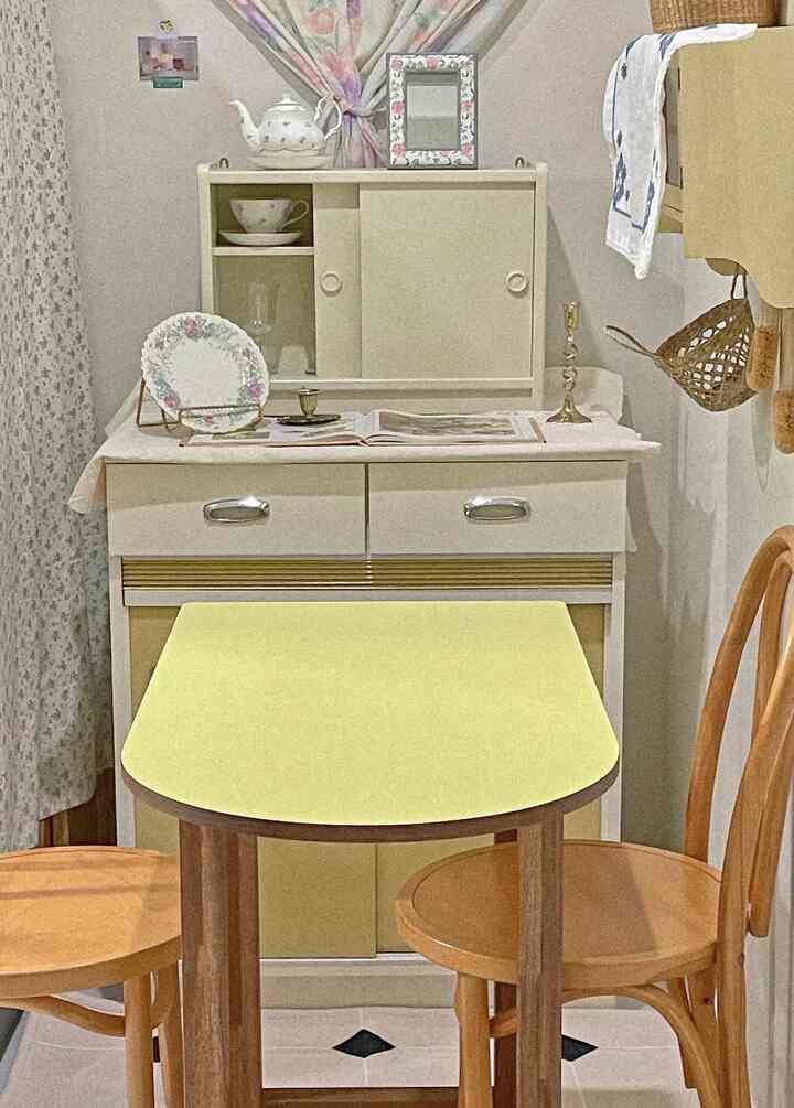 黄色と茶色のトーンが特徴のコンパクトなダイニングルーム、木製のテーブルと椅子、レトロな食器と装飾品が配置された印象的な空間