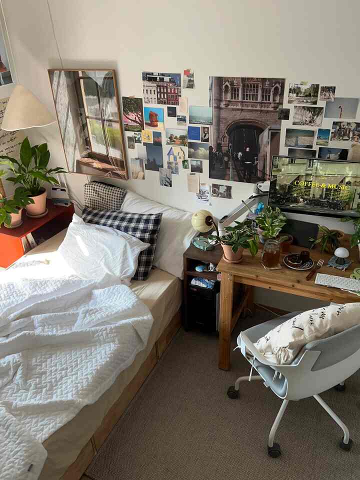 Cozy bedroom with white bedding, wood-tone desk, and plants arranged, featuring a natural atmosphere and compact home office setup