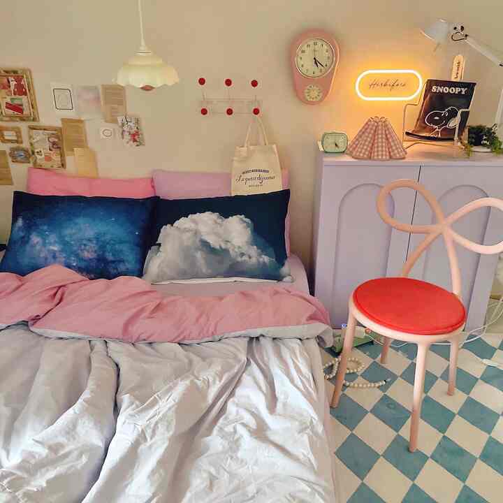 Pink and white toned bedroom featuring cloud and galaxy pillows, cozy space with vibrant wall decor