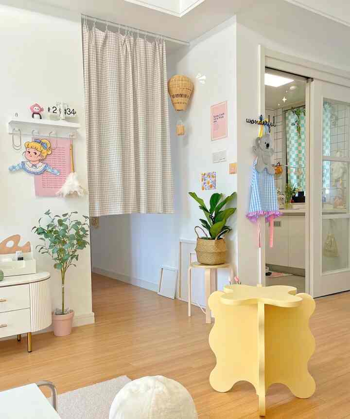 Bright natural-toned living room featuring wooden flooring, beige checkered curtain, yellow stool, and plant stands creating cozy charm