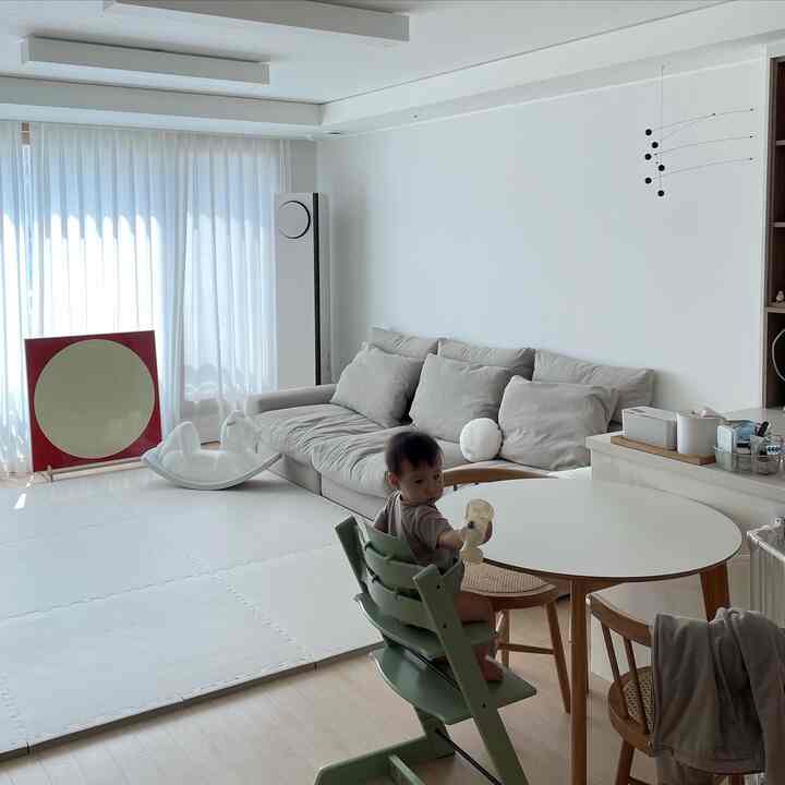 ホワイトと木目調が調和したリビング、ダイニングチェアに座る赤ちゃんと吊るされたモビールが配置された自然な雰囲気のインテリア