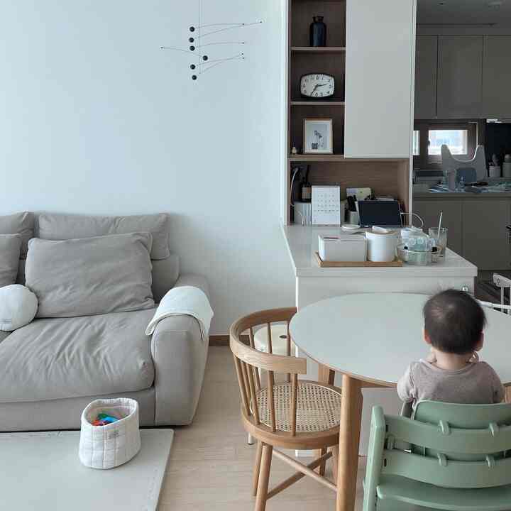 明るくナチュラルモダンでウッドトーンのリビングとキッチン、円形のダイニングテーブルとベビー椅子が配置された家族向けの雰囲気あるインテリア