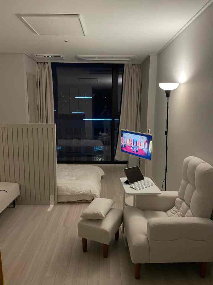 A bright white and natural tone studio bedroom featuring a recliner, blackout curtains, and TV stand in a cozy atmosphere