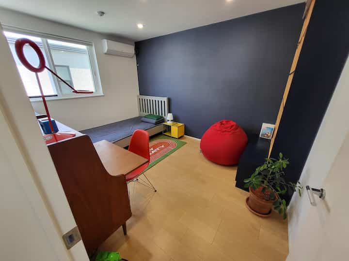 ネイビーブルーのアクセントウォールと木目調の床が特徴的な子供部屋、赤いビーンバッグ、デスク、ベッドが配置されたミッドセンチュリーモダンなインテリア