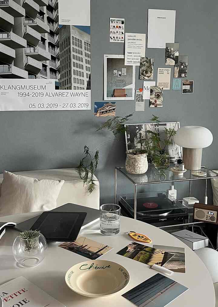 Natural styled studio apartment with gray walls, white round table, single armchair, plants, and a table lamp