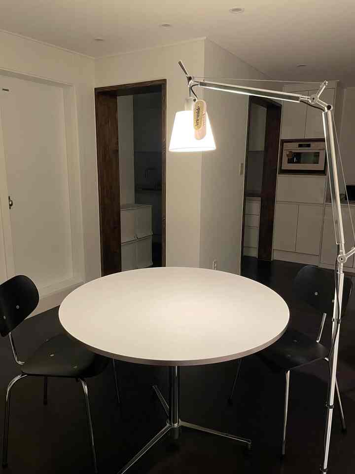 A modern small studio living dining room in white and black tones featuring a round dining table, black chairs, and an Artemide floor lamp