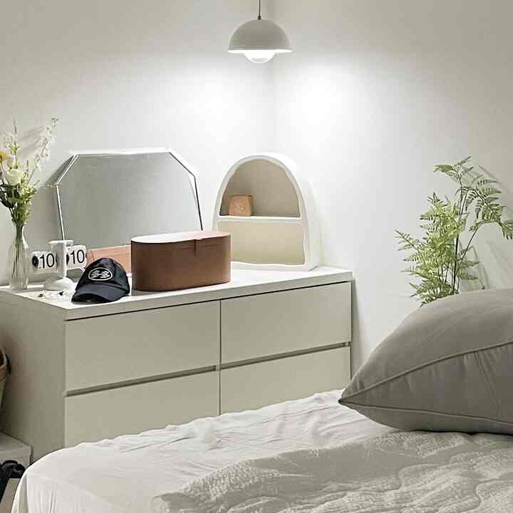 White-toned bedroom featuring a central white dresser and a bed with pillows and bedspread creating a clean atmosphere