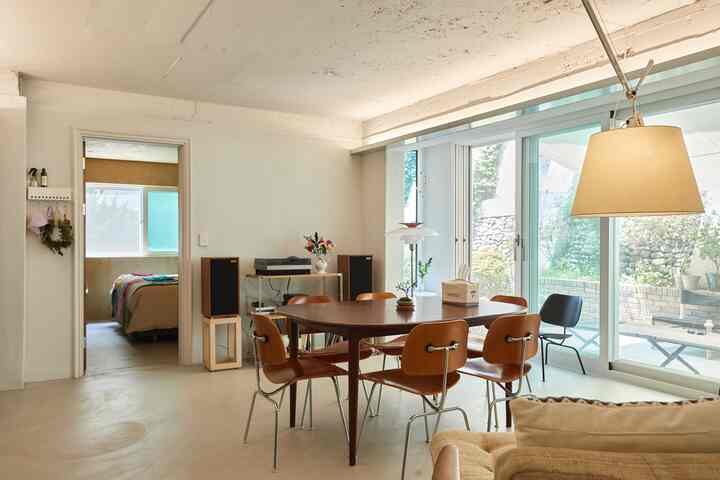 Bright white-walled mid-century modern dining room with wood tone dining table and chairs, featuring natural lighting and plant decor creating a cozy ambiance