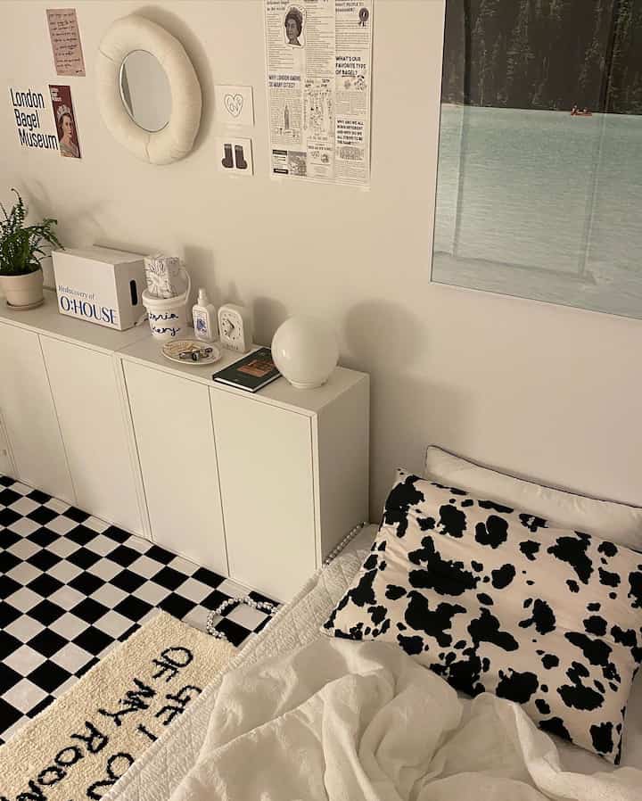 Monotone bedroom space in white and black featuring a checkered carpet and large sofa pillow with a simple interior design