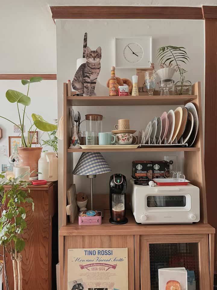 Natural color wood-tone kitchen dining room featuring cat figurine, coffee machine, and decorative shelves in a cozy setting