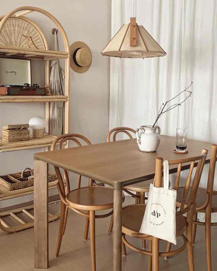Natural tone dining room featuring wood tone dining table and chairs, rattan shelf, beige curtains and lighting creating a cozy atmosphere