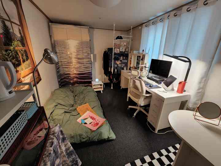 白と黒のトーンのワンルーム、一人用ベッドとデスク、オフィスチェアが配置された在宅勤務の空間