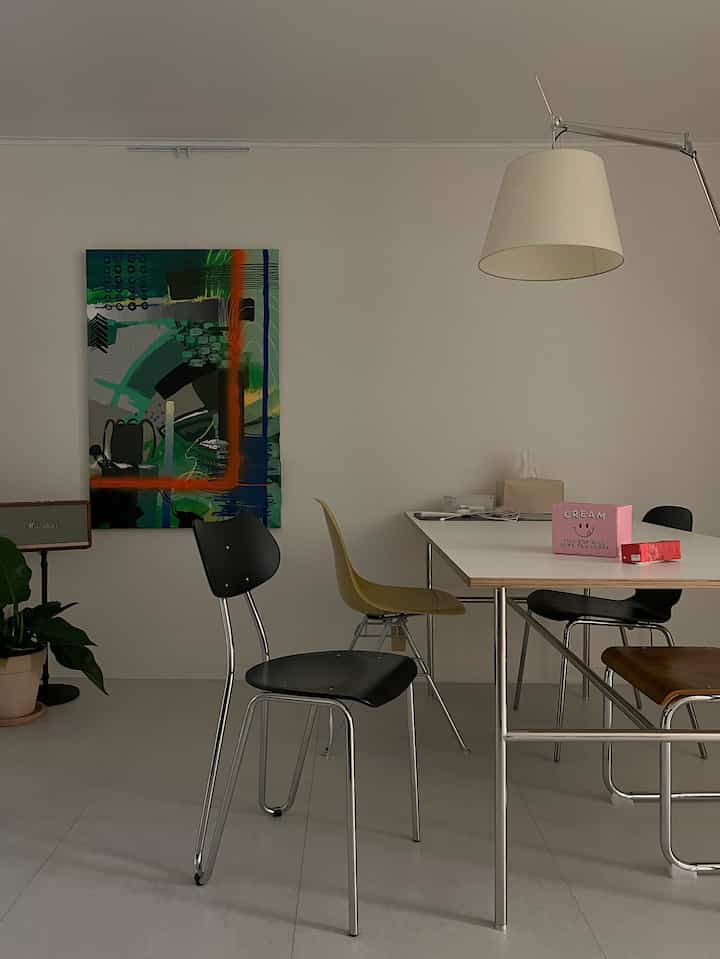 White-toned dining room featuring diverse chairs and large wall art in a modern setting