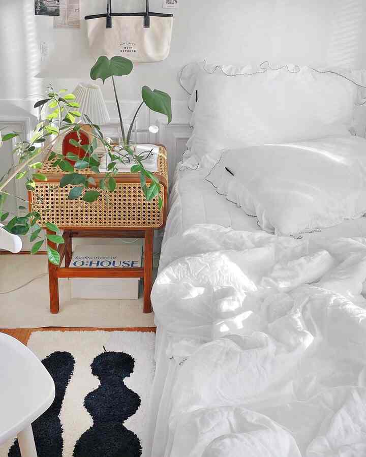 Bright white-toned bedroom featuring rattan storage table and frill pillows creating cozy natural ambiance