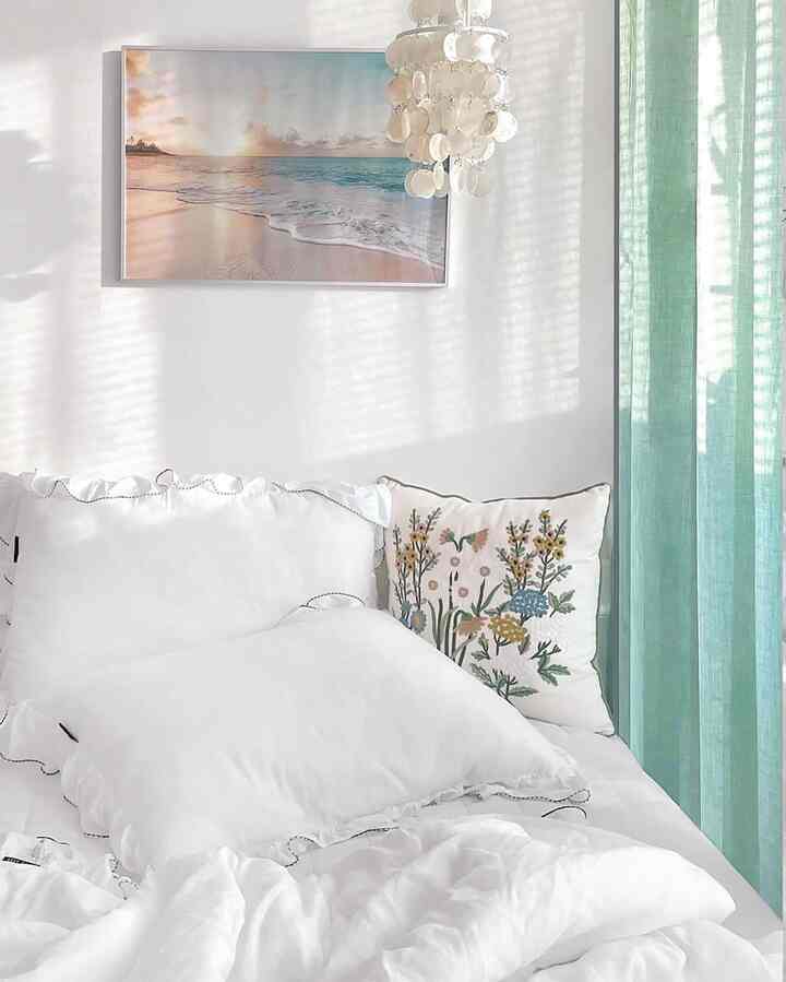 A white and mint toned bedroom featuring white bedding and floral embroidered cushions creating a clean, natural space