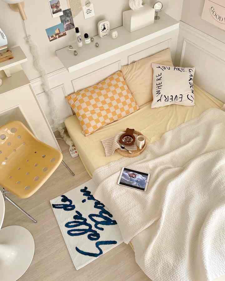 White and yellow-toned bedroom featuring pillows and blanket on bed, conveying a cozy atmosphere