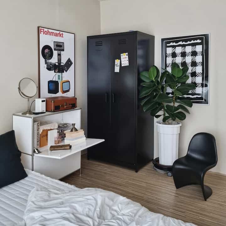 Black and white toned bedroom featuring a central cabinet closet, bed and a large plant, creating a modern atmosphere