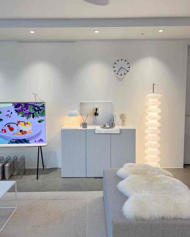 Minimalist living room in white and gray tones featuring sofa, clock, and lighting with a clean, calm atmosphere