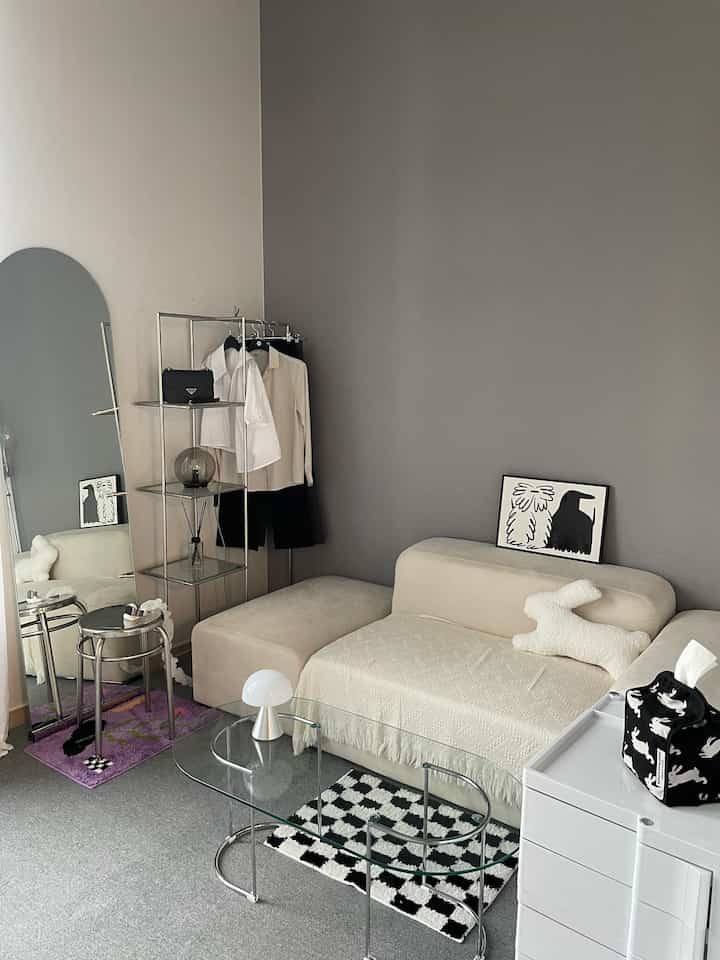 Studio living room with gray walls and carpet, beige sofa and glass coffee table creating a modern atmosphere