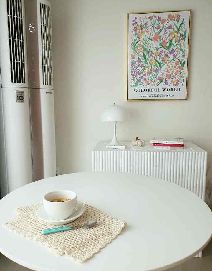 Simple interior in white and beige tones featuring a round dining table, white table lamp, and floral picture frame with cozy atmosphere