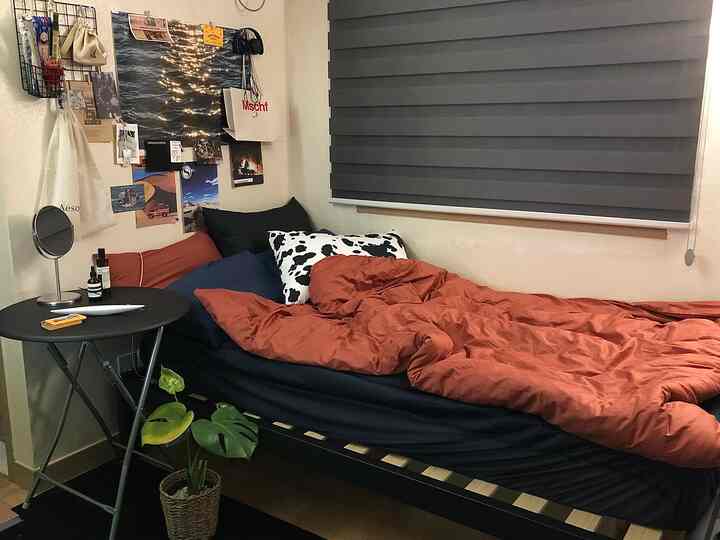 暖かみのあるブラウンとブルーのトーンの狭い寝室、ベッドとナイトテーブル、ブラインド、観葉植物が配置された雰囲気のあるインテリア