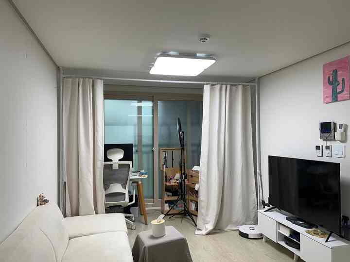 白とベージュのトーンのワンルーム新婚宅リビング、ソファとカーテンで空間を仕切った実用的なホームオフィスが配置された居心地の良い空間