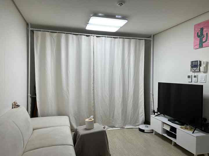 白とベージュのトーンのワンルームリビング、カーテンとソファ、テレビ台が配置されたシンプルな空間