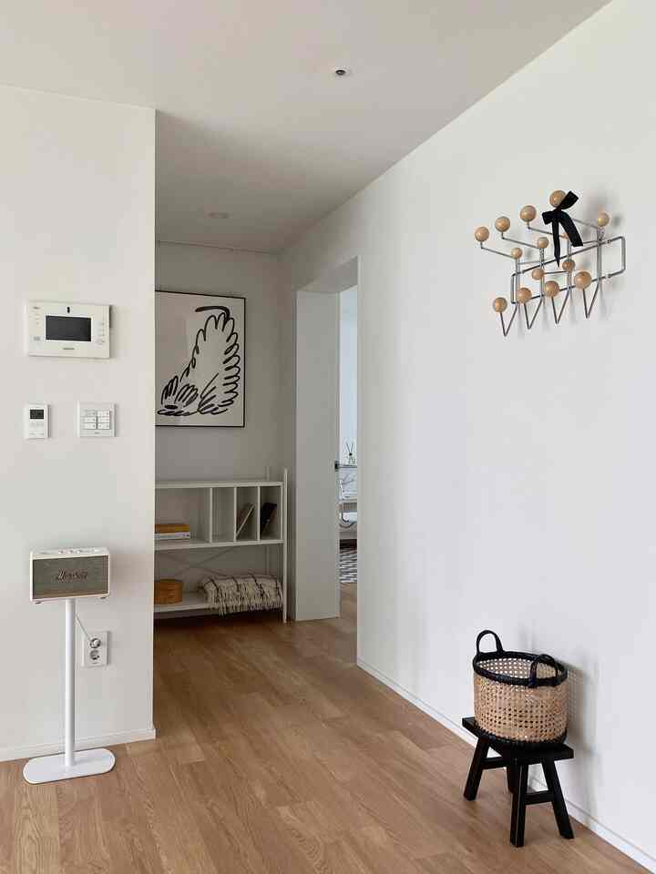 Bright white walls and natural wood-tone flooring in a hallway space featuring a wall-mounted coat rack and open shelving for storage