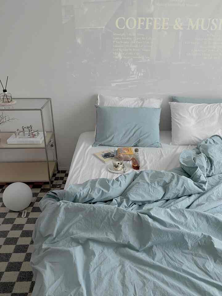 柔らかなブルーとホワイトのトーンの寝室、中央に寝具と枕が配置されたカフェ風の落ち着いたインテリア