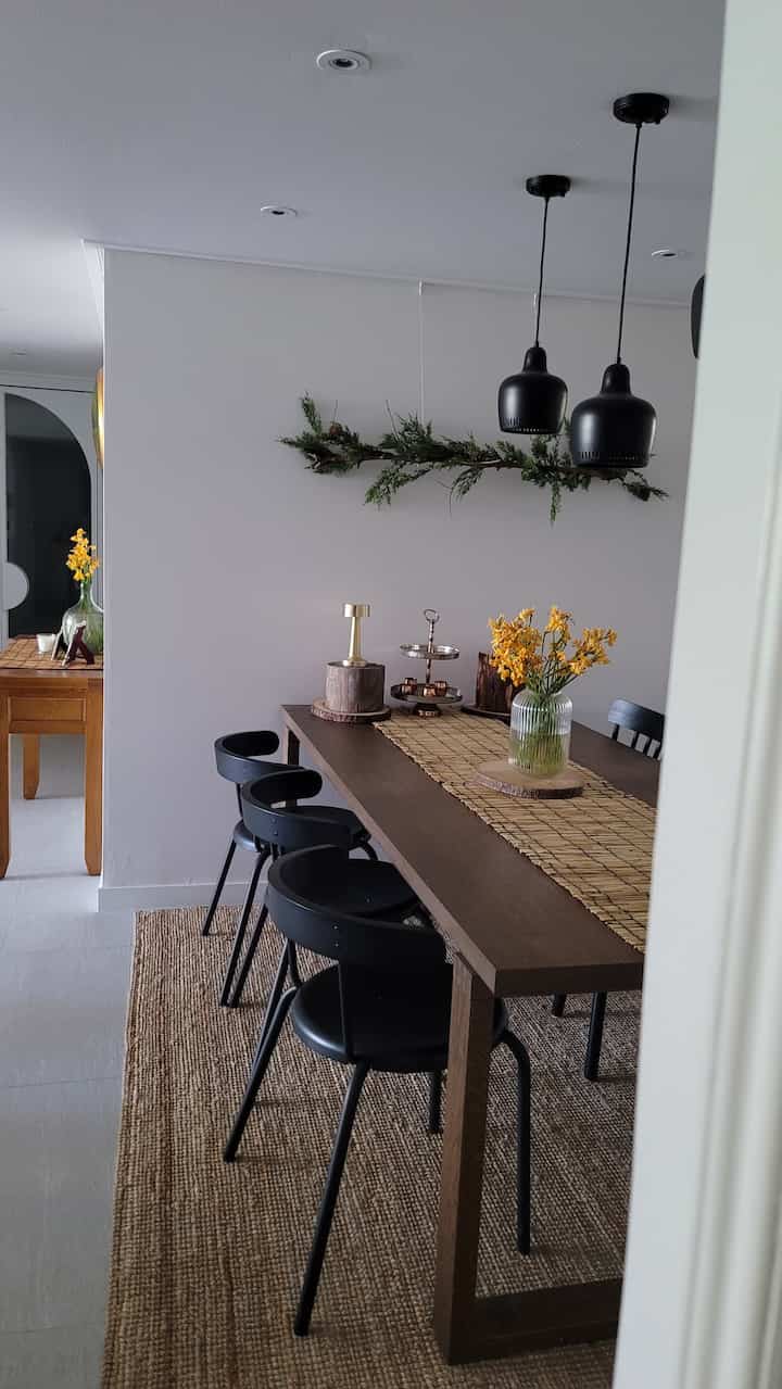 ブラウンと黒の色調のダイニングルーム、長いダイニングテーブルと黒い椅子、黄色い花と自然素材の装飾が配置された雰囲気のある空間