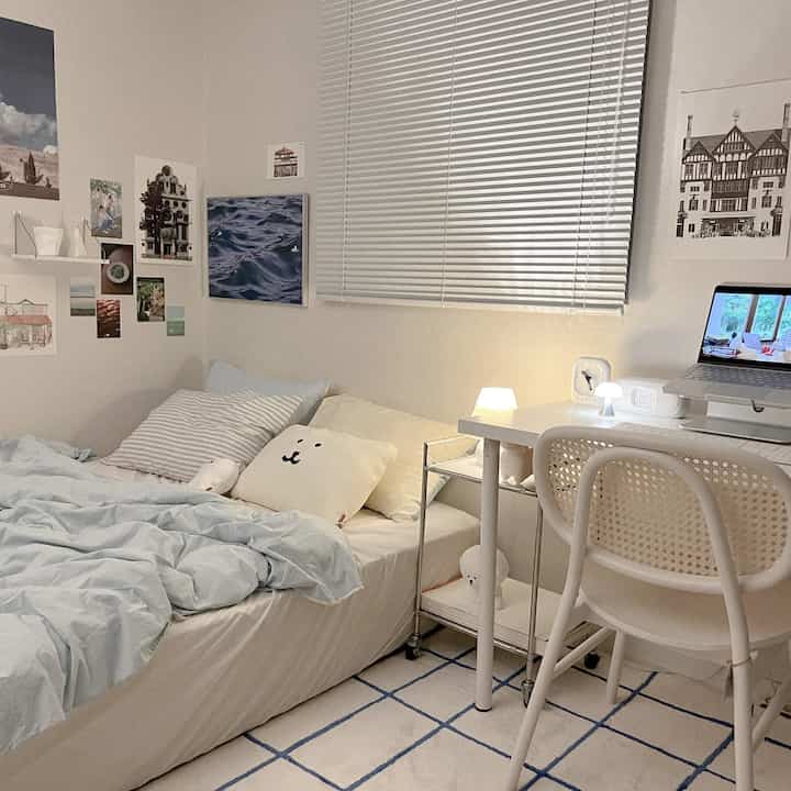 A calm blue and white toned bedroom featuring a bed, desk, and posters creating a cozy and organized atmosphere