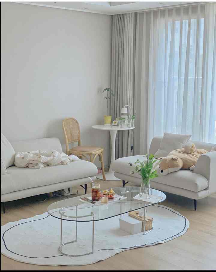 A clean and cozy living room in white and beige tones featuring transparent glass coffee table and light-colored sofas