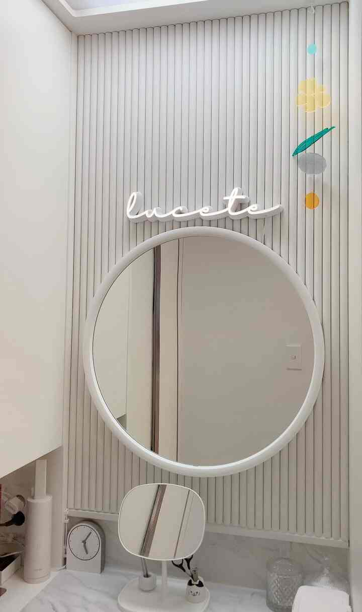 ホワイトトーンのパウダールーム、ラウンドミラーとすっきりとしたモールディングが配置されたミニマルな空間